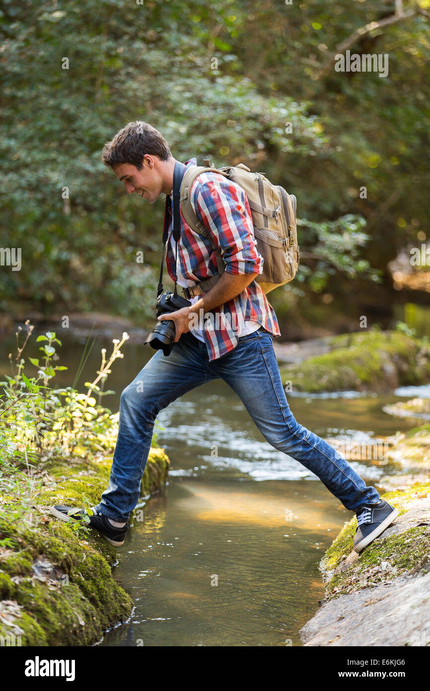 young photographer crossing water stream at mountain valley Stock Photo