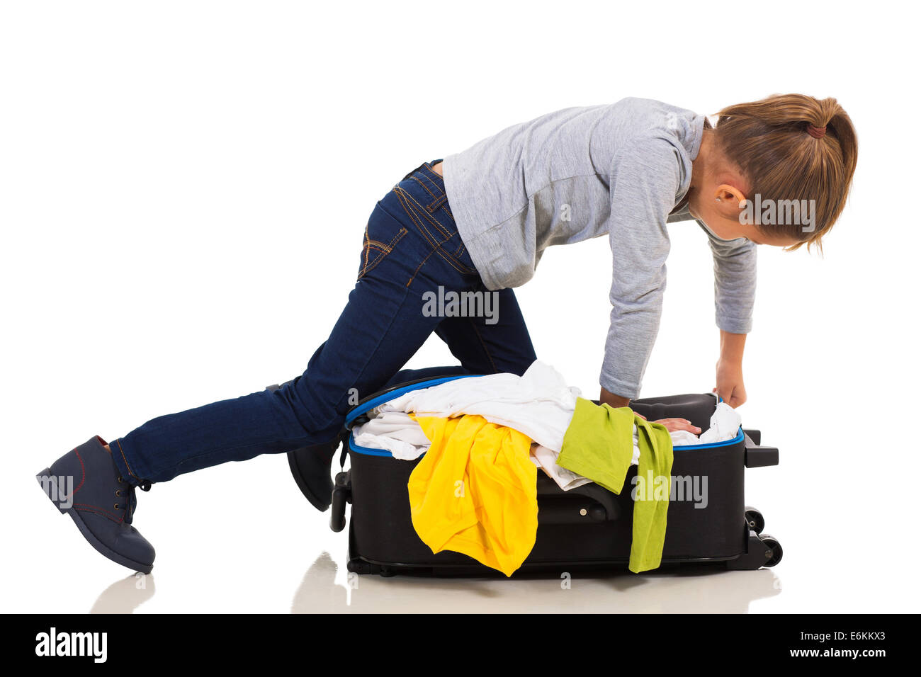young girl kneeing on suitcase trying to zip it up Stock Photo
