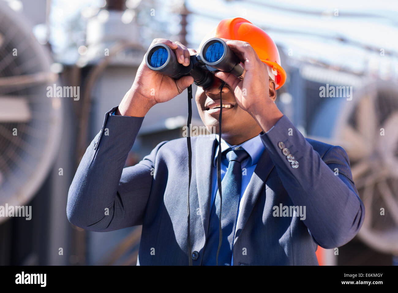 African electrician engineer using binoculars looking at electricity substation Stock Photo