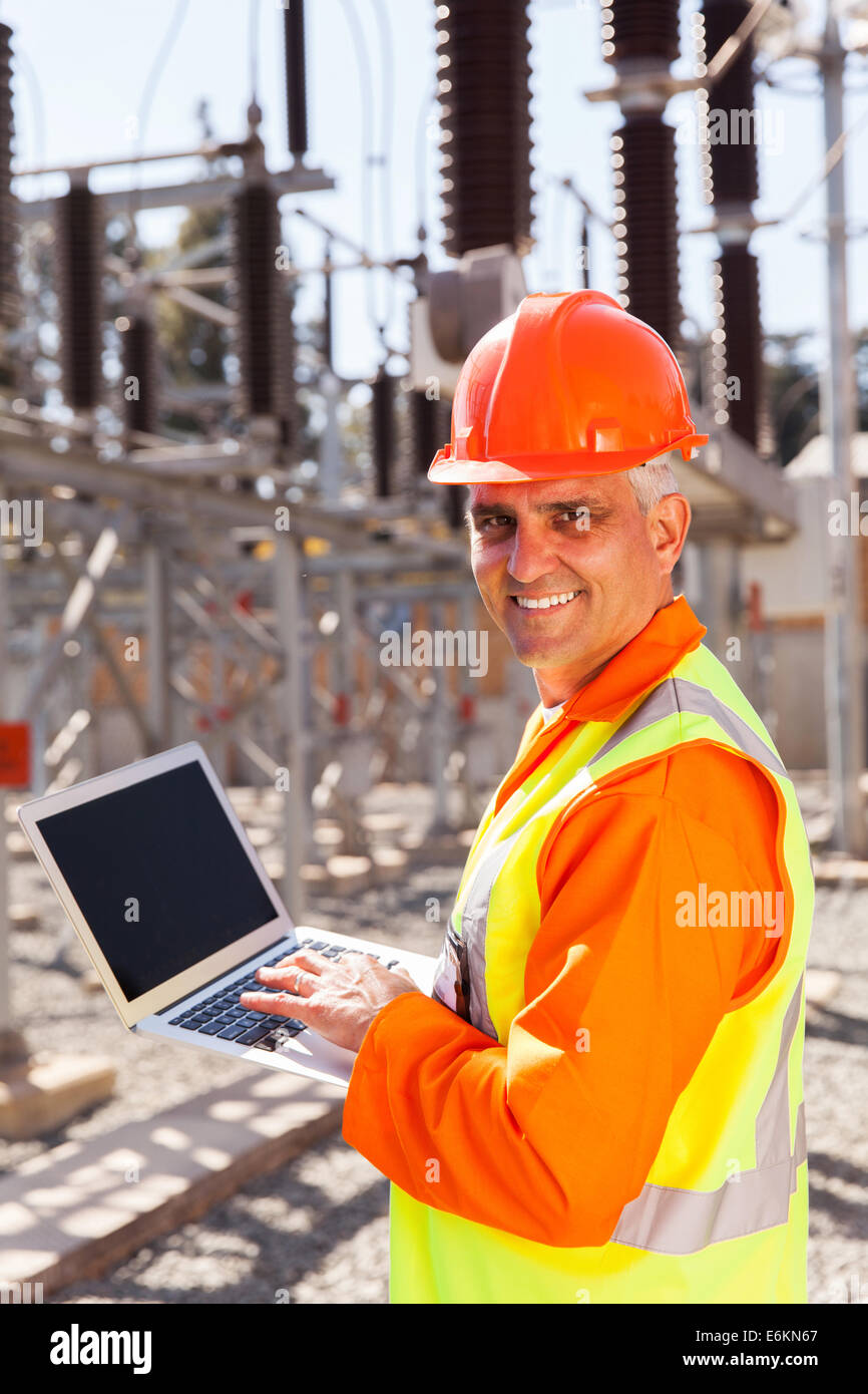 smiling senior electrician using laptop in substation Stock Photo