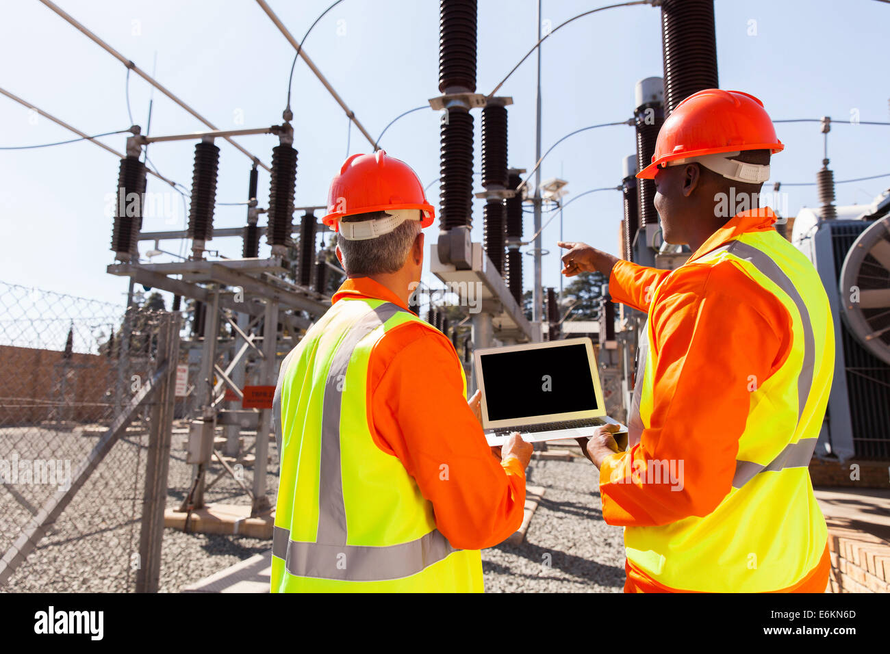 rear view of electricians with laptop pointing in substation Stock ...