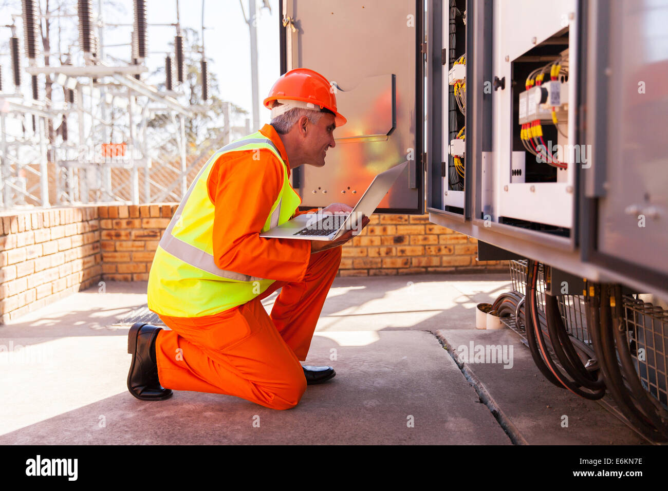 successful mid age electrician kneeing in front of transformer Stock Photo