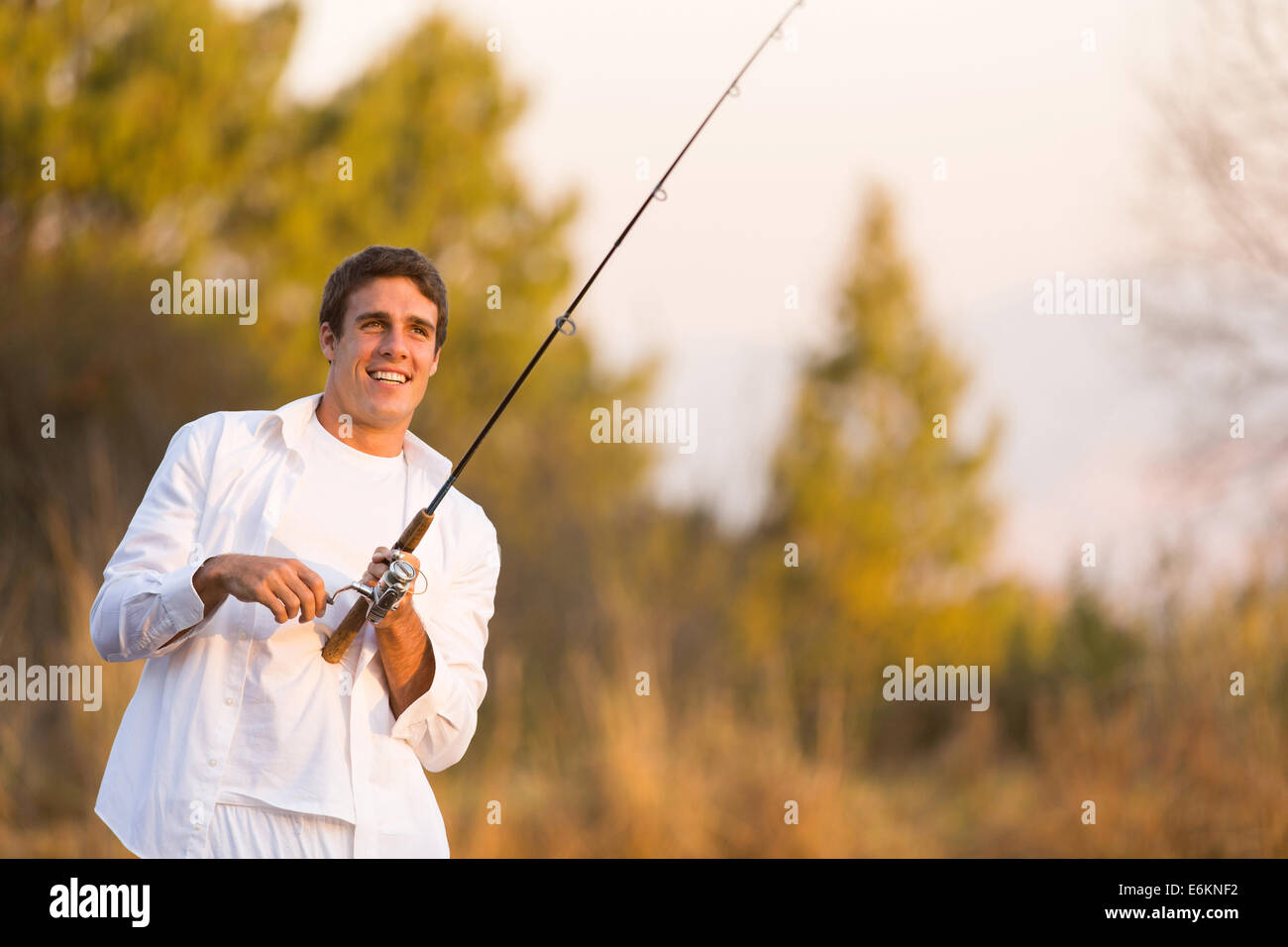 happy young man catching a fish with rod by the lake Stock Photo