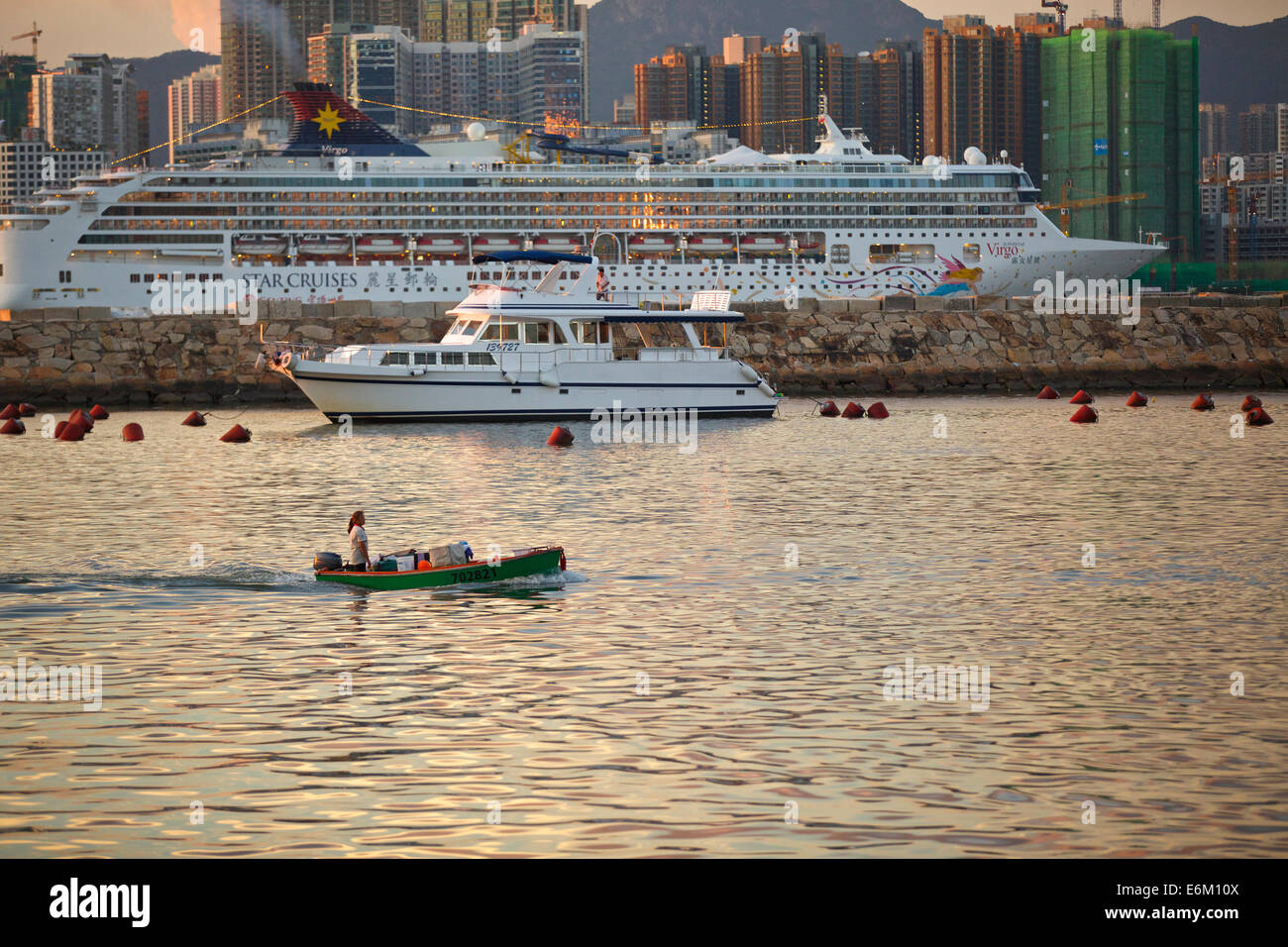 Contrasting Vessels. Small Boat In The Causeway Bay Typhoon Shelter And A Cruise Ship Passing Through Victoria Harbour, Hong Kong Skyline Behind. Stock Photo