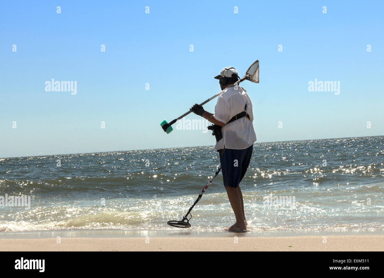man at beach shoreline with metal detector Stock Photo