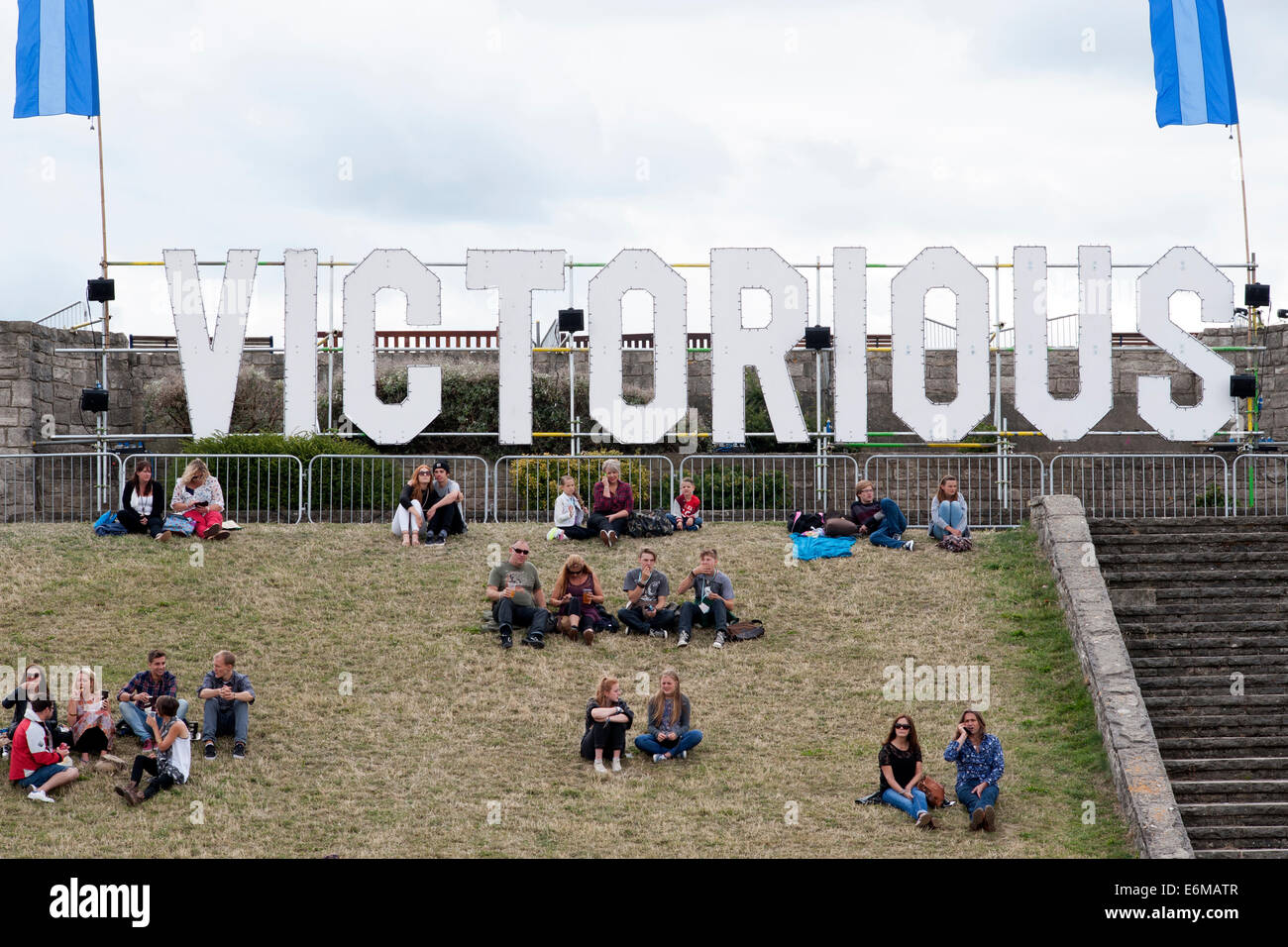 festival goers sat on a grass bank beneath large victorious sign at the victorious festival 2014 southsea england uk Stock Photo