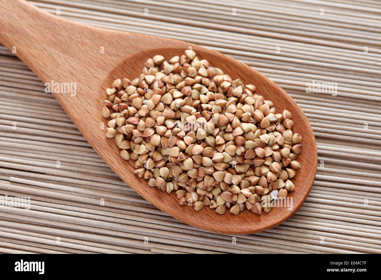 Raw buckwheat in a wooden spoon on soba noodles background. Stock Photo