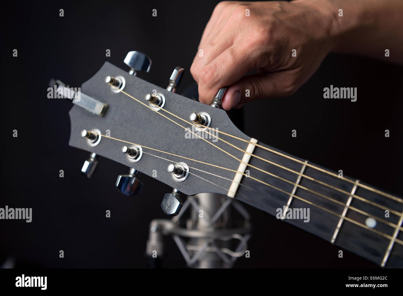 Close-up of a hand turning a guitars tuning pegs with a studio microphone in the background. Stock Photo