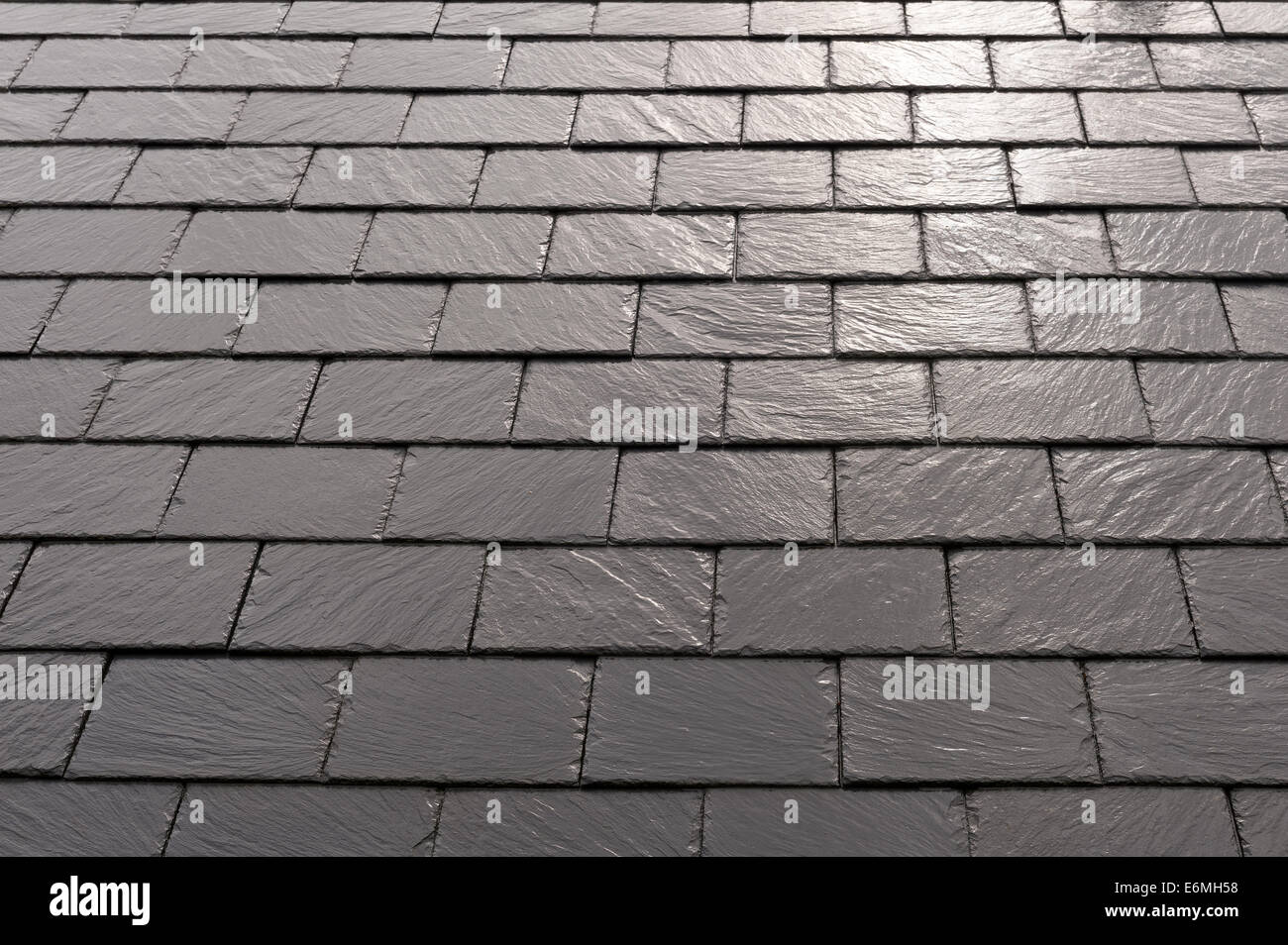 Wet rain covered new slate tiles laid in regular rows on roof with burst sunlight reflecting from shiny slates damp conditions Stock Photo