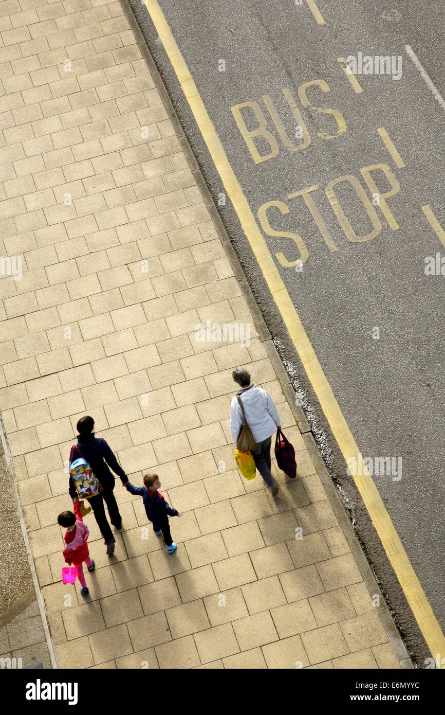 Adults and children walking alongside an empty bus stop. Stock Photo
