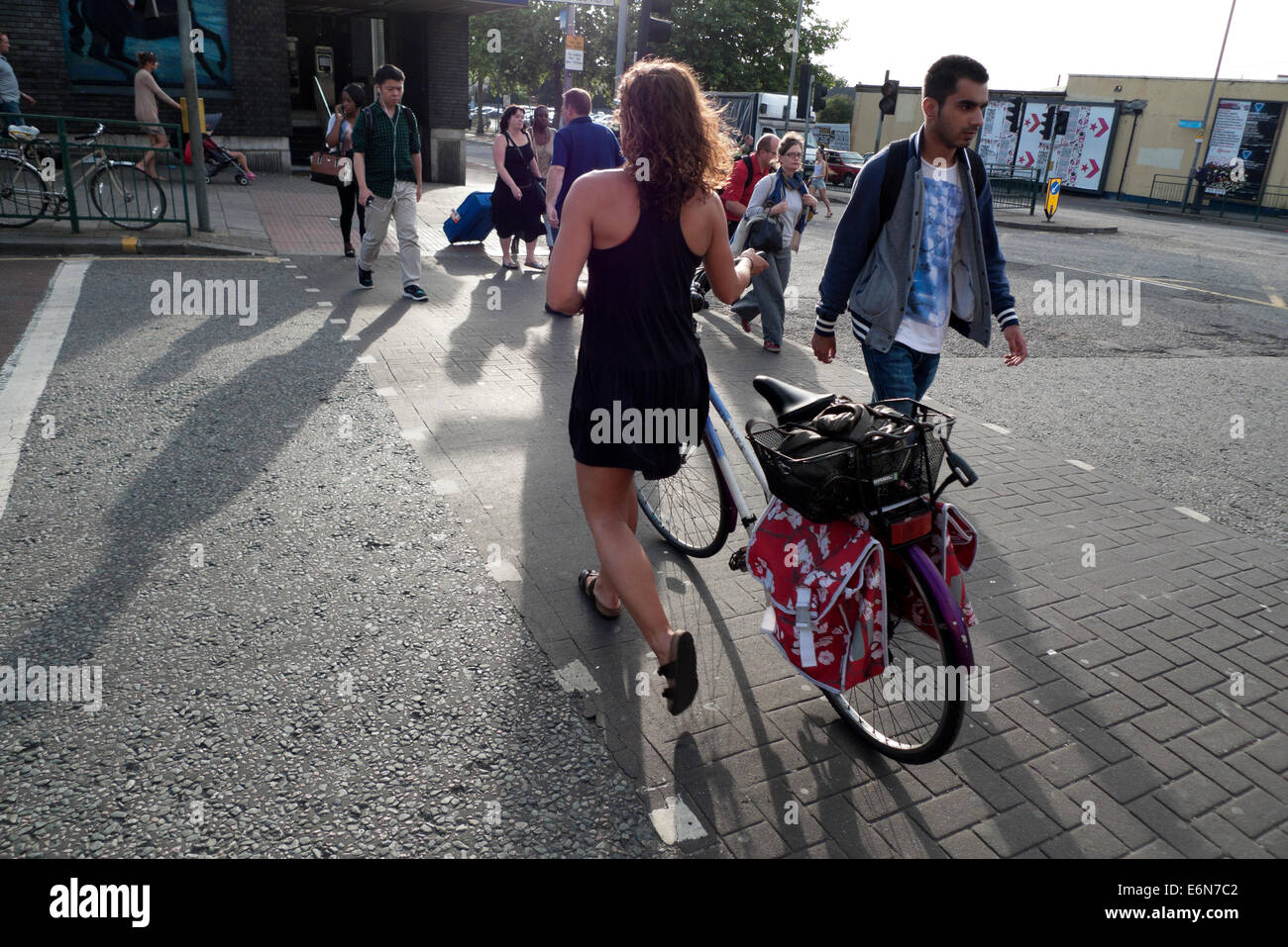 Woman with vintage bicycle in summer viewed from behind crossing the road near Blackhorse Road tube station Walthamstow London E17 UK  KATHY DEWITT Stock Photo