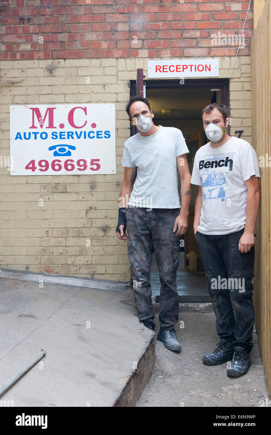 Marshgate, Swindon, Wiltshire, UK. 27 August 2014. Malcolm Curwen and son of M.C. Auto Services wear face masks in an attempt to minimise any toxic effects of the acrid smoke from the burning pile of waste at Averies Recycling, right next door to their business. The waste has been smouldering since 21 July 2014 and the fire is now being tackled by firefighters from Swindon, Marlborough, Royal Wooton Bassett and elsewhere in Wiltshire. Photograph Credit:  2014 John Henshall / Alamy Live News. JMH6381 Stock Photo