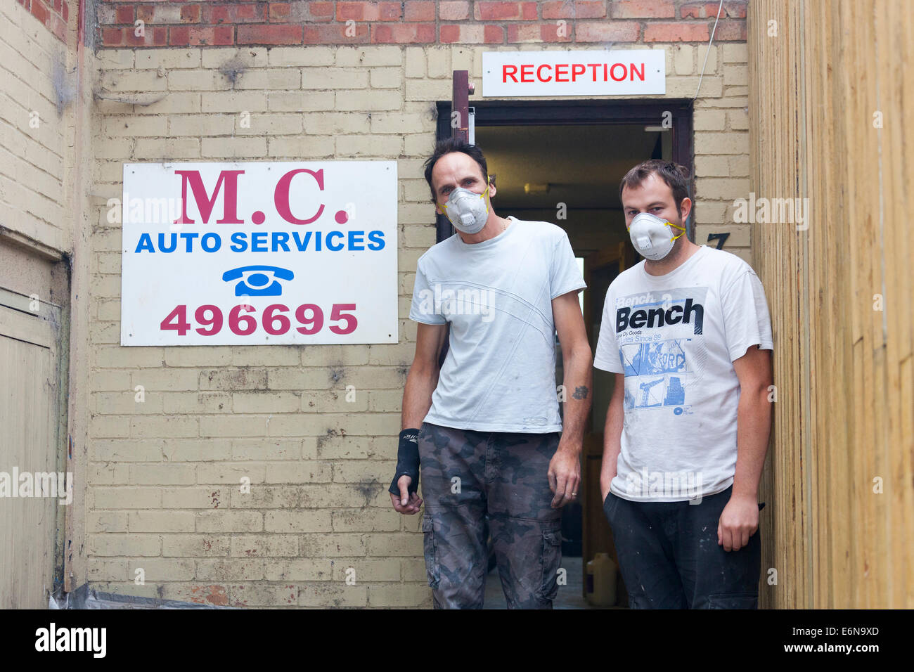 Marshgate, Swindon, Wiltshire, UK. 27 August 2014. Malcolm Curwen and son of M.C. Auto Services wear face masks in an attempt to minimise any toxic effects of the acrid smoke from the burning pile of waste at Averies Recycling, right next door to their business. The waste has been smouldering since 21 July 2014 and the fire is now being tackled by firefighters from Swindon, Marlborough, Royal Wooton Bassett and elsewhere in Wiltshire. Photograph Credit:  2014 John Henshall / Alamy Live News. JMH6382 Stock Photo