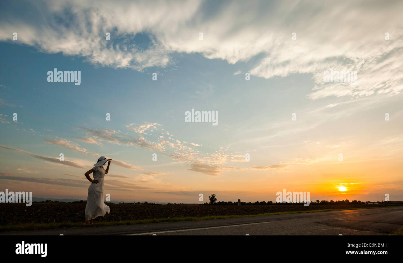 Woman in white dress and white hat staying on in the street looking ...