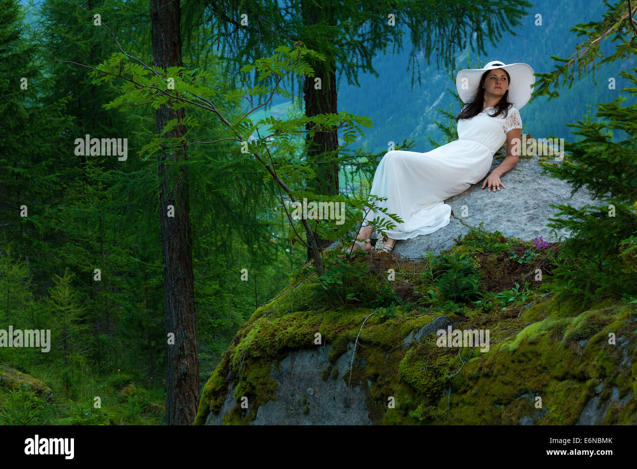Caucasian woman in white dress with white hat lying on a big stone in ...