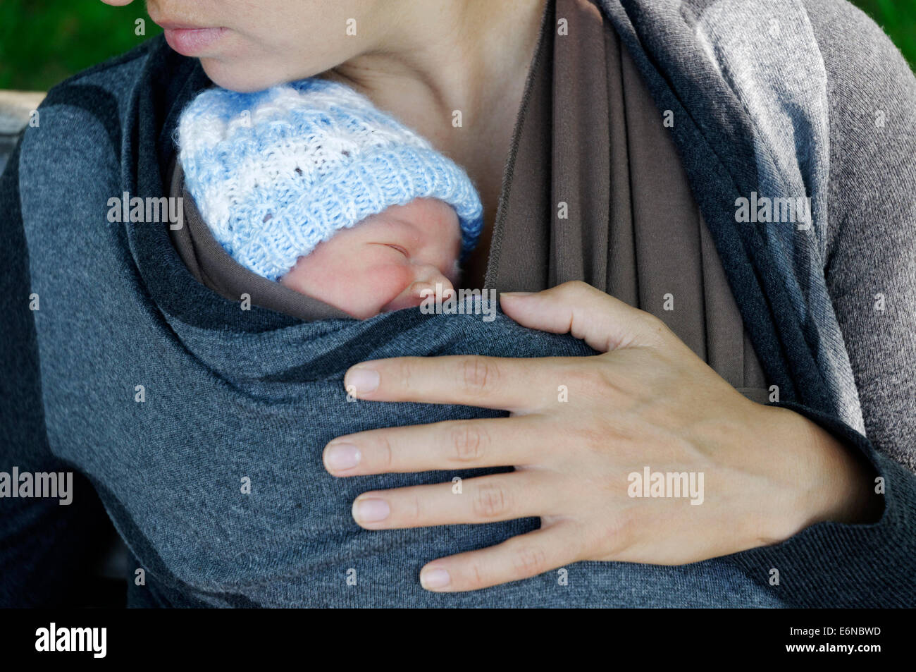A newborn baby asleep in a baby carrier wrap being held by the mother Stock Photo