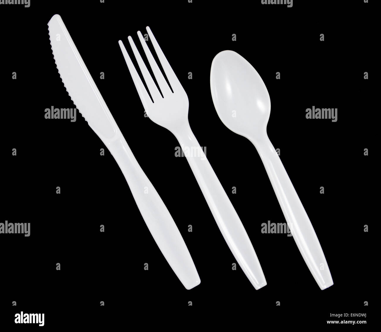 White plastic knife, fork and spoon on black background. Stock Photo