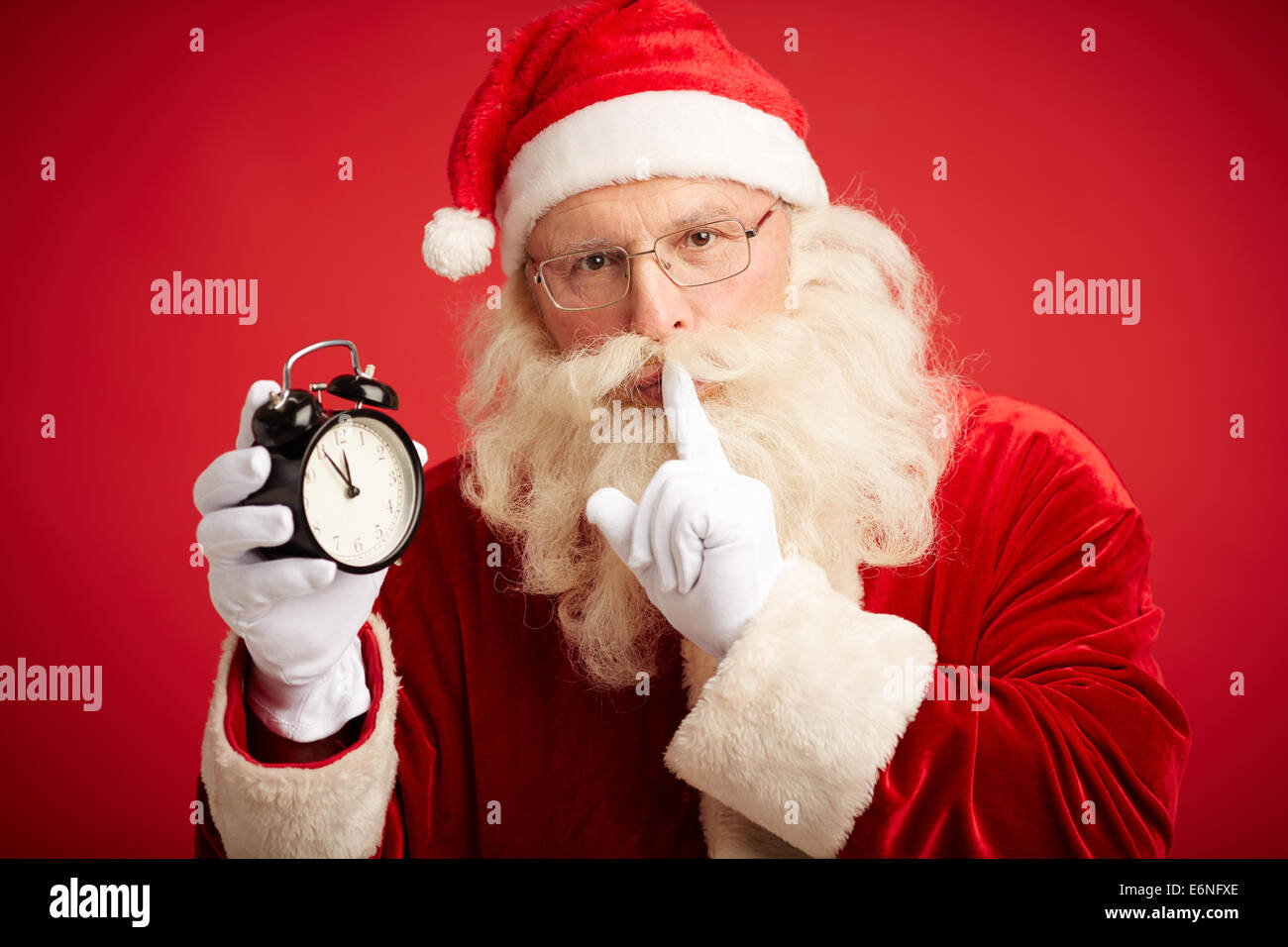 Santa Claus holding clock showing five minutes to midnight and making shhh gesture Stock Photo