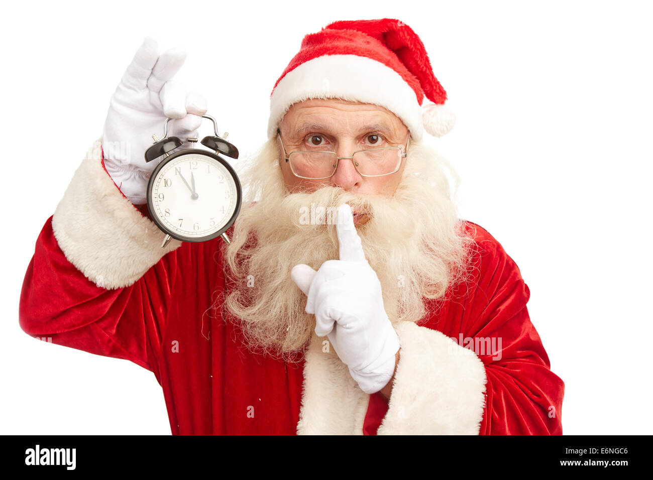 Santa Claus with alarm clock showing five minutes to midnight making shhh gesture and looking at camera Stock Photo