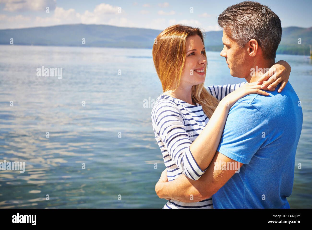 Amorous man and woman standing in embrace by lake Stock Photo