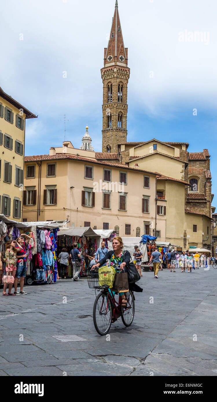 Woman riding a bicycle down a street with market stalls and tourists shopping in Florence, Italy. Stock Photo