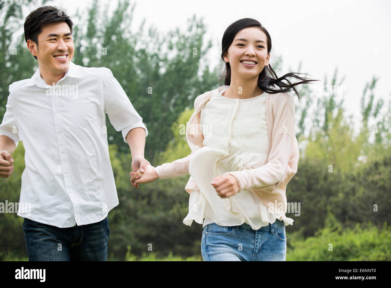 Happy young couple holding hands running Stock Photo - Alamy