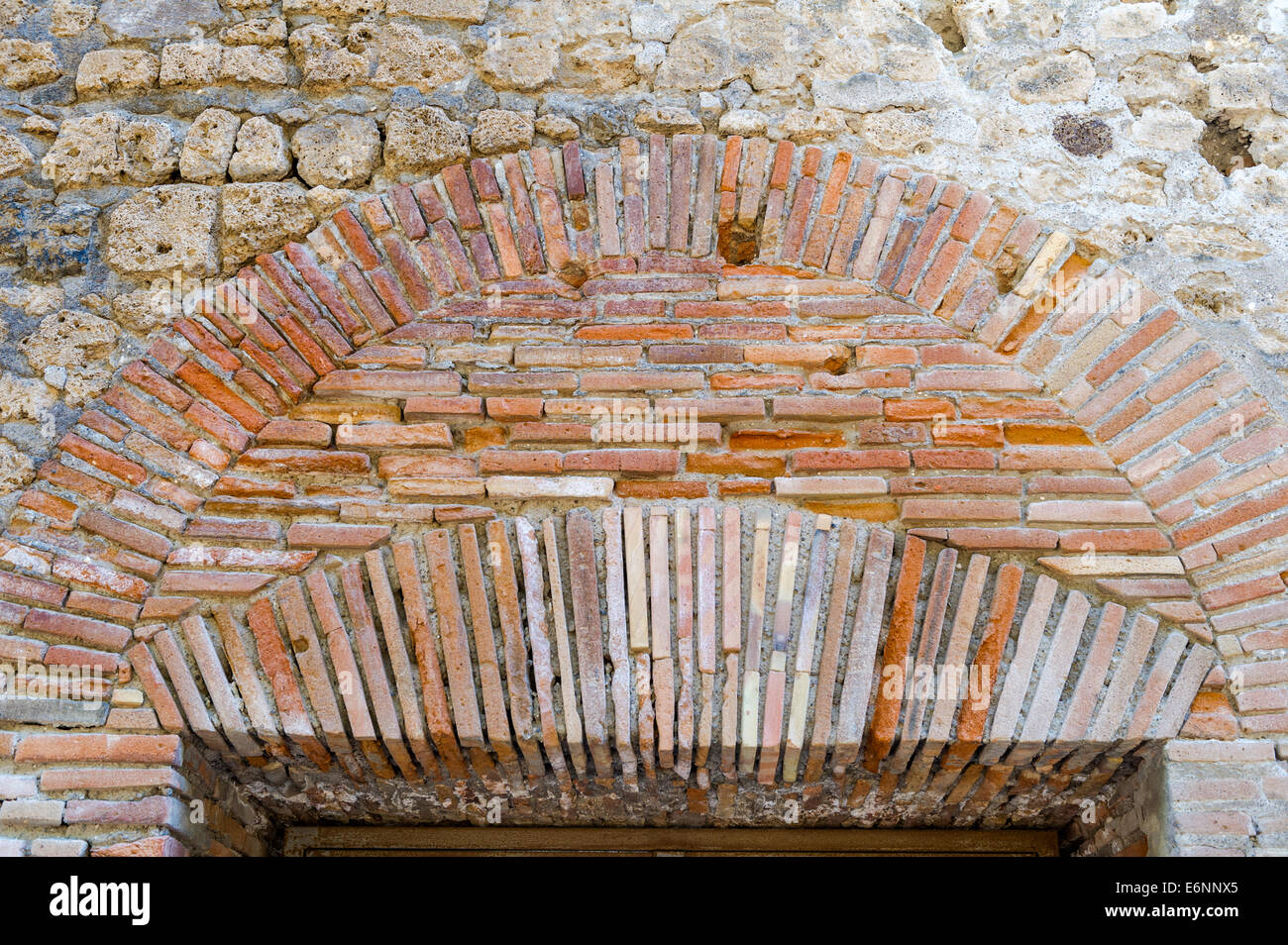 Stone, brick and clay tiles forming the archway over a door entrance to a ruined house in the roman city of Pompeii. Stock Photo