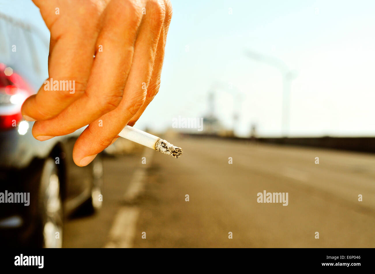closeup of a man with a burning cigarette in his hand while is waiting besides a car parked next to a no traffic road Stock Photo