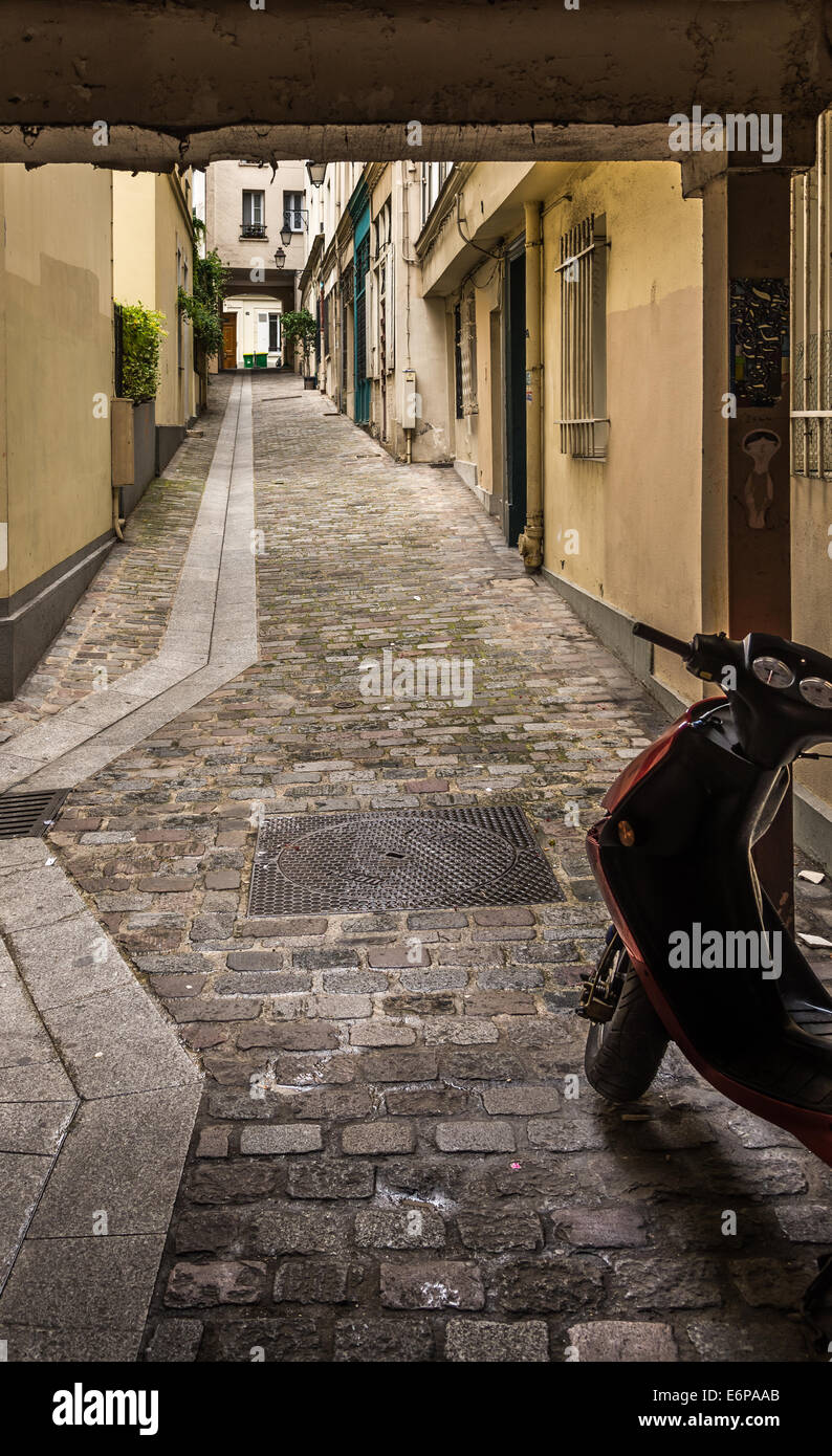 A motor bike sits in the shadow at the entrance to a cobble stone lane. Stock Photo