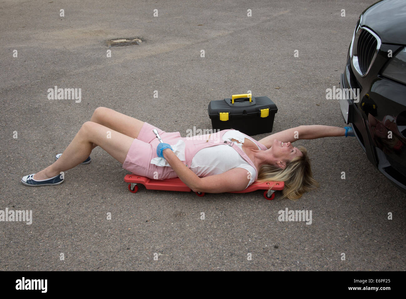 Working on a car female motor mechanic laying on a crawler to gain access under a car Stock Photo