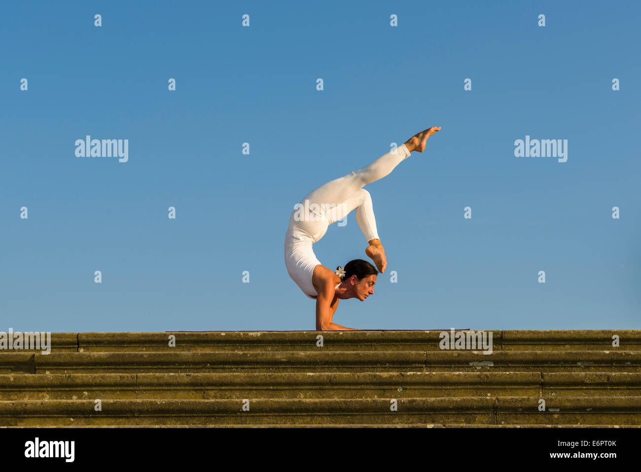 Young woman practising Hatha yoga, outdoors, showing the pose Vrischikasana, Scorpion pose Stock Photo