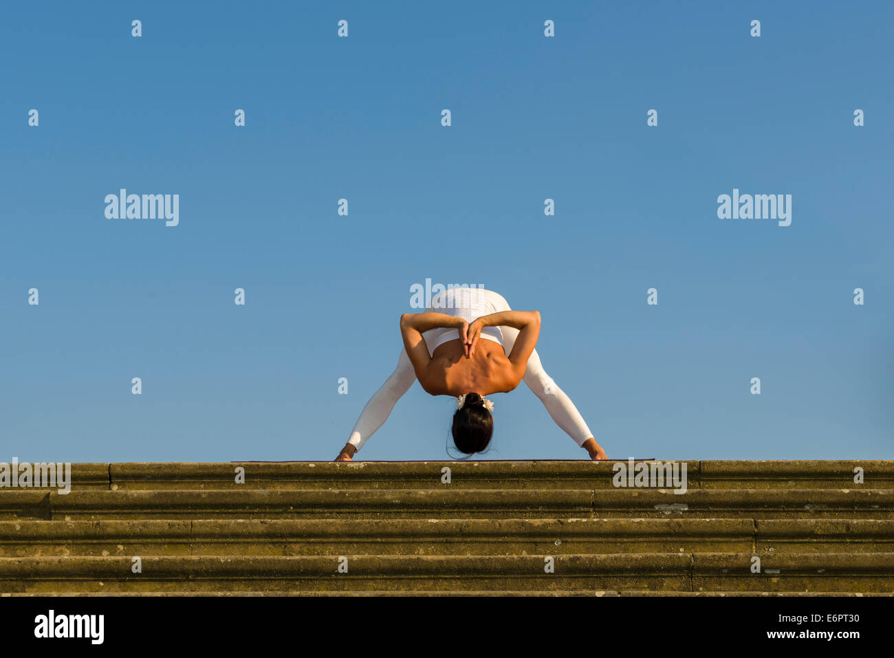 Young woman practising Hatha yoga, outdoors, showing the pose Prasarita padottanasana, Wide-legged forward bend Stock Photo