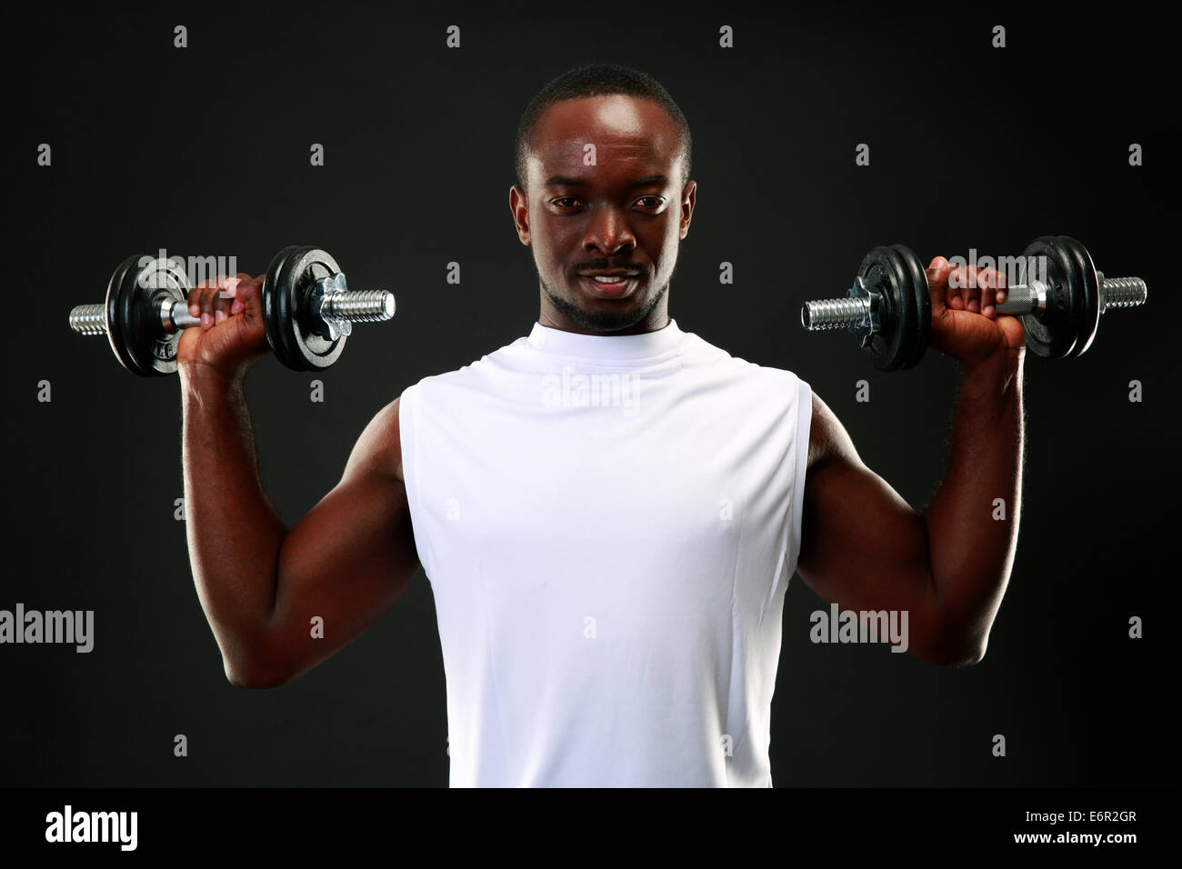 Portrait of a happy african man with dumbbells over black background ...