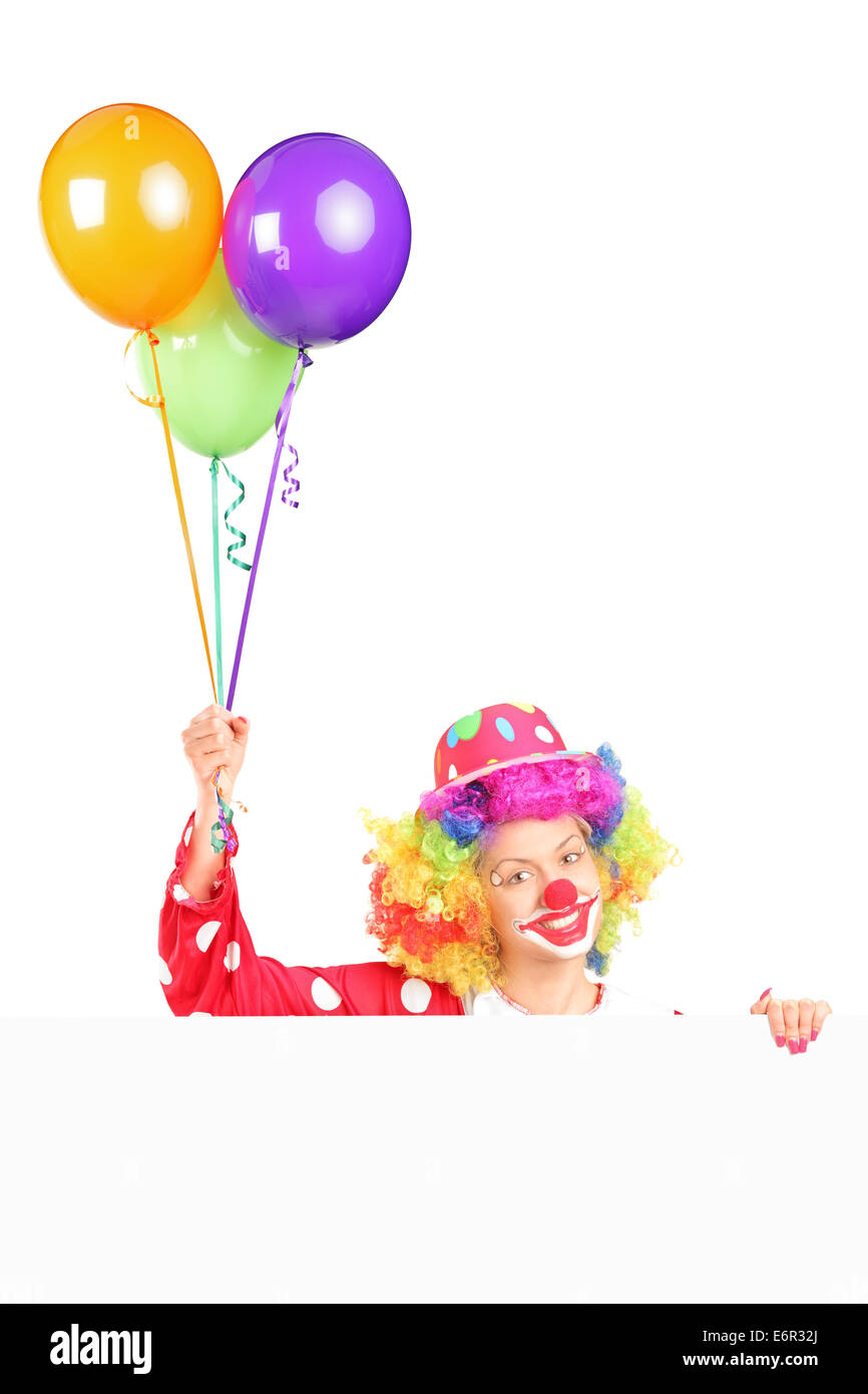 Female clown holding balloons behind a panel isolated on white ...