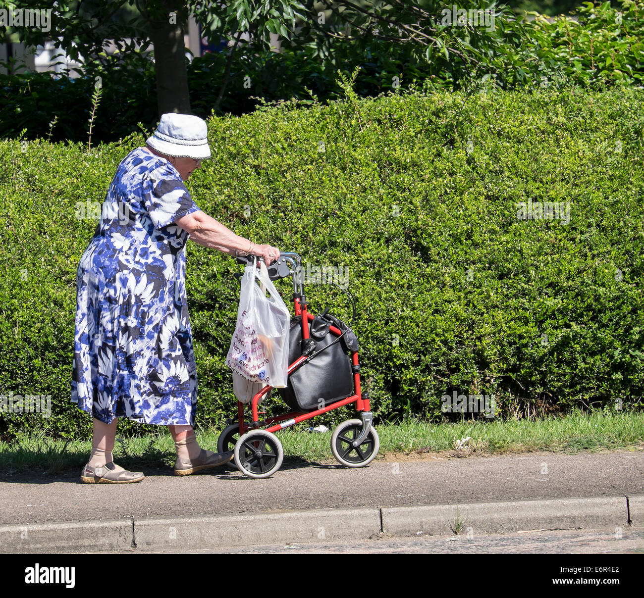 Elderly lady walking with aid of wheeled shopper trolley Stock Photo