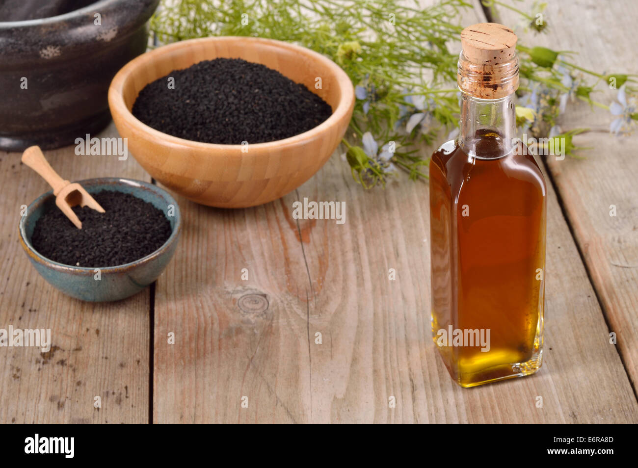 Nigella sativa oil in a bottle and nigella seeds and flowers on wooden background. Black cumin healing herb. Cold pressed, non r Stock Photo