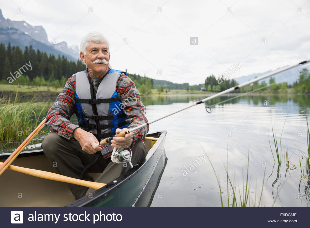 Older man fishing in canoe in still lake Stock Photo