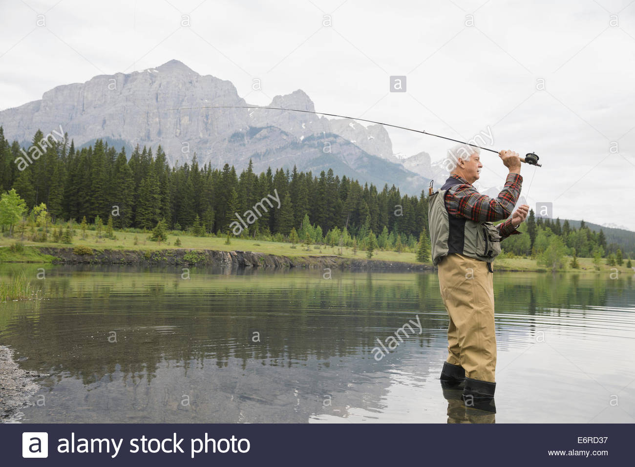 Older man fishing in still lake Stock Photo