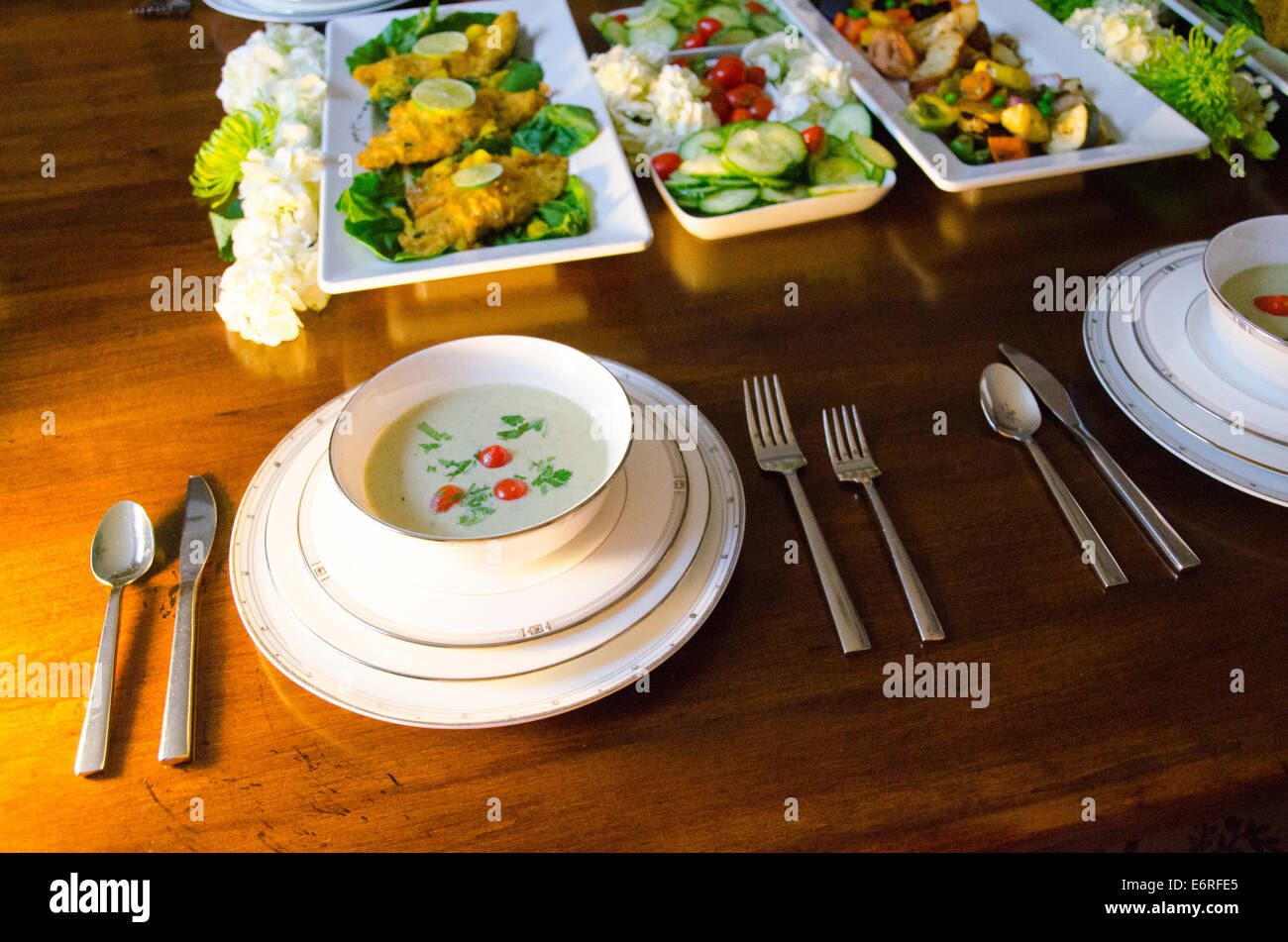 Buffet style dinner party in an elegant setting with soup, fish and vegetables on a wooden dining table with fancy white china Stock Photo