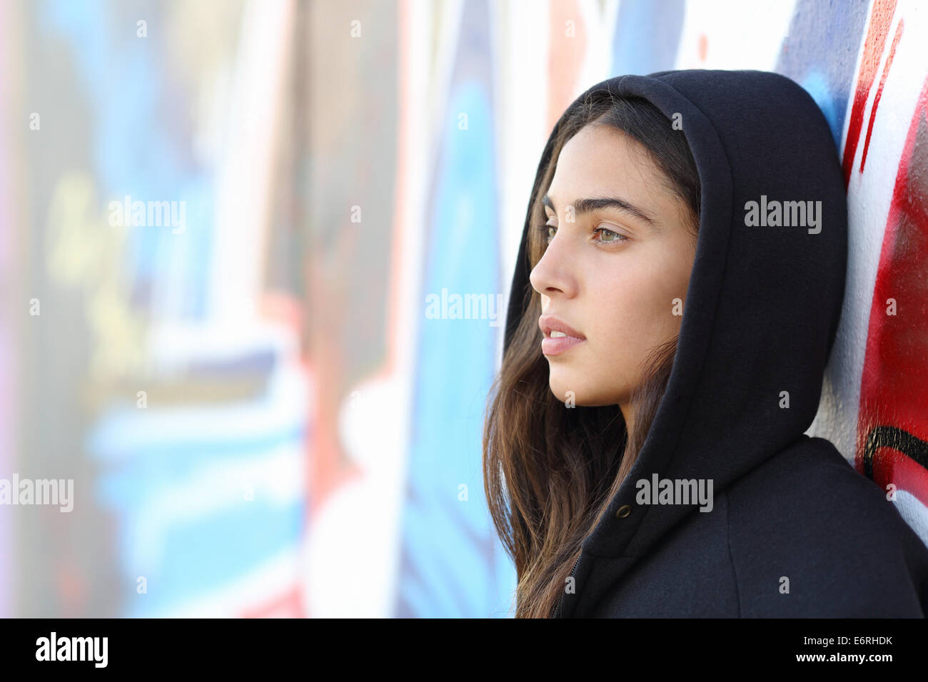 Profile portrait of a skater style teenager girl with an unfocused graffiti wall in the background Stock Photo