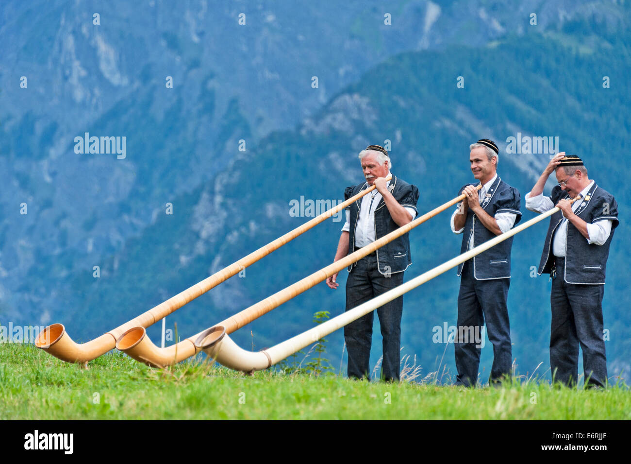 A Swiss alphorn trio, dressed in National costume, preparing to play their instruments, against a background of the Alps. Stock Photo