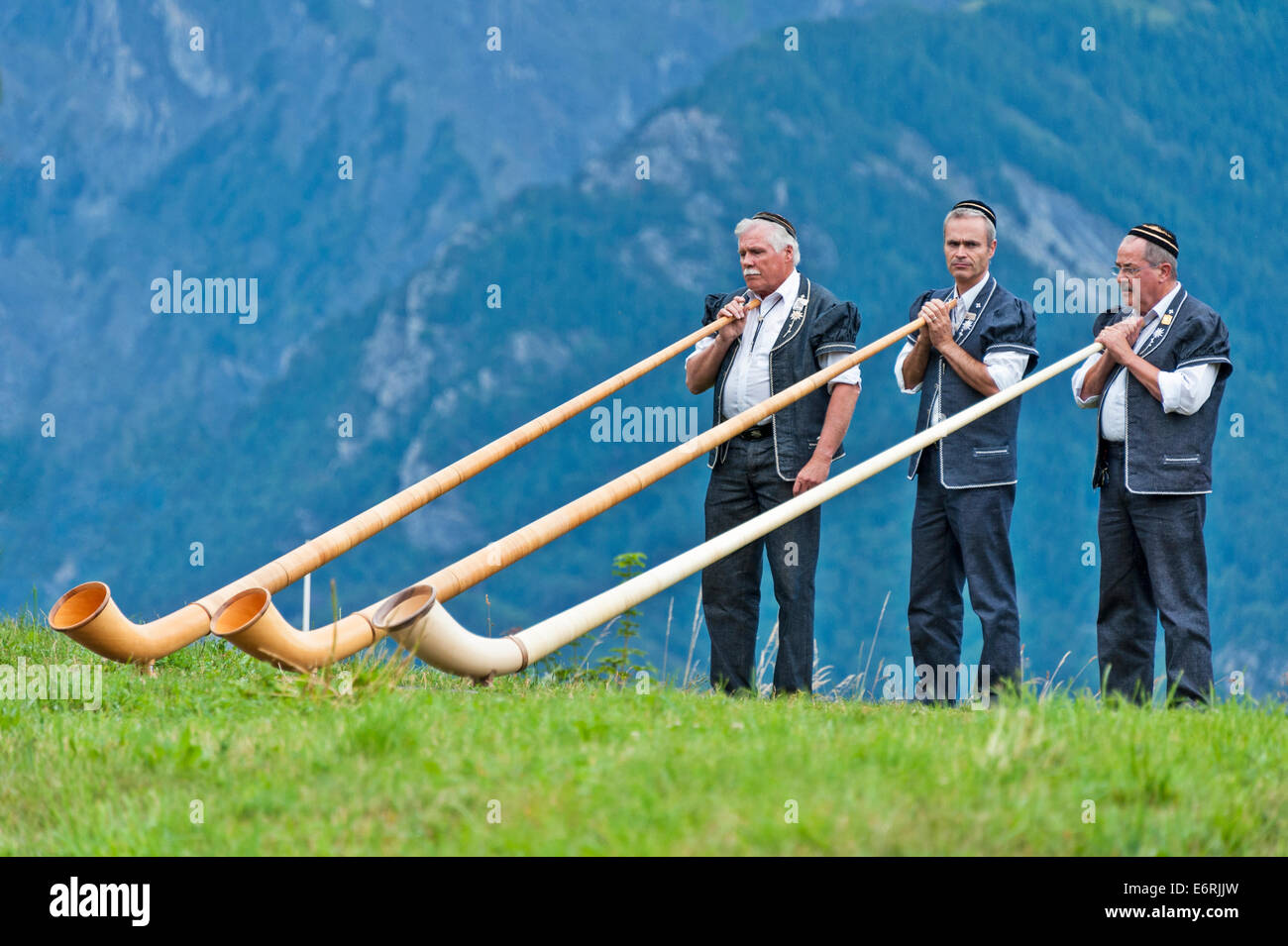 Three Swiss alphorn players, wearing traditional dress, preparing to play their instruments Stock Photo