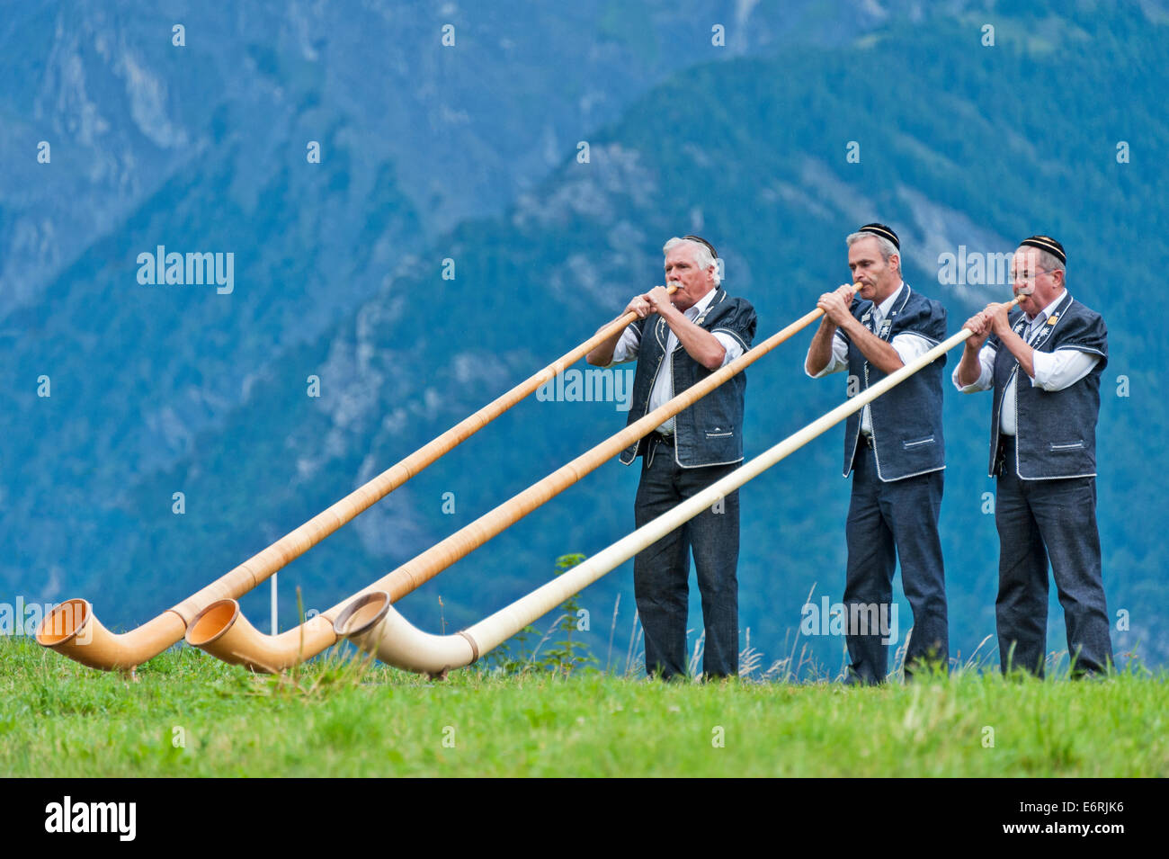 Three Swiss alphorn players against a background of mountains. Stock Photo