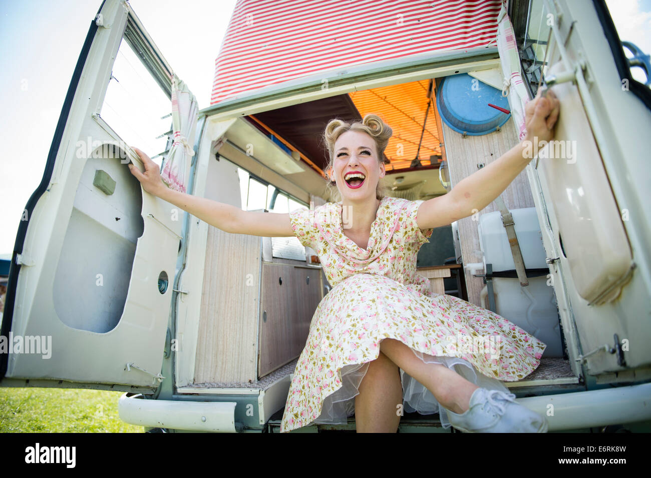 A woman dressed in retro 50's American housewife style summer dress frock sitting posing in a classic period camper van UK Stock Photo