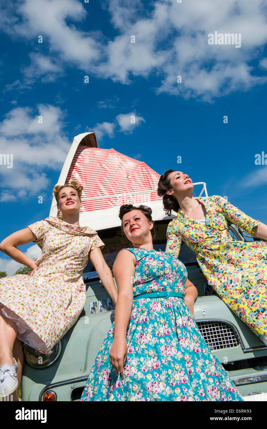 Three women dressed in retro 50's American housewife style floral flowery bright colourful cotton summer dresses frocks posing with a camper van Stock Photo