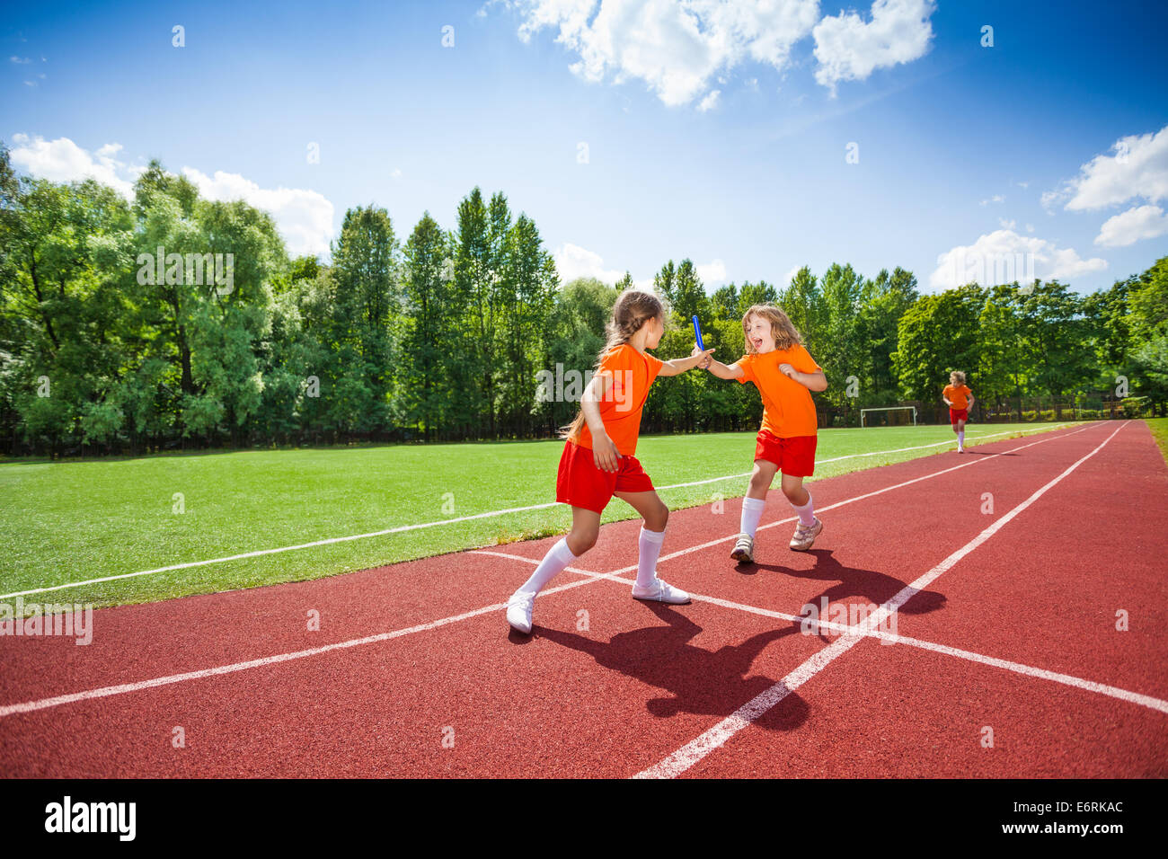 Girl with baton runs and hands it to other runner Stock Photo