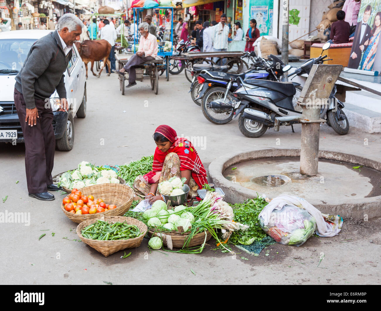 Street scene in Deogarh, Rajasthan, India: young woman dressed in sari sitting in the road sells fresh vegetables to passers-by Stock Photo