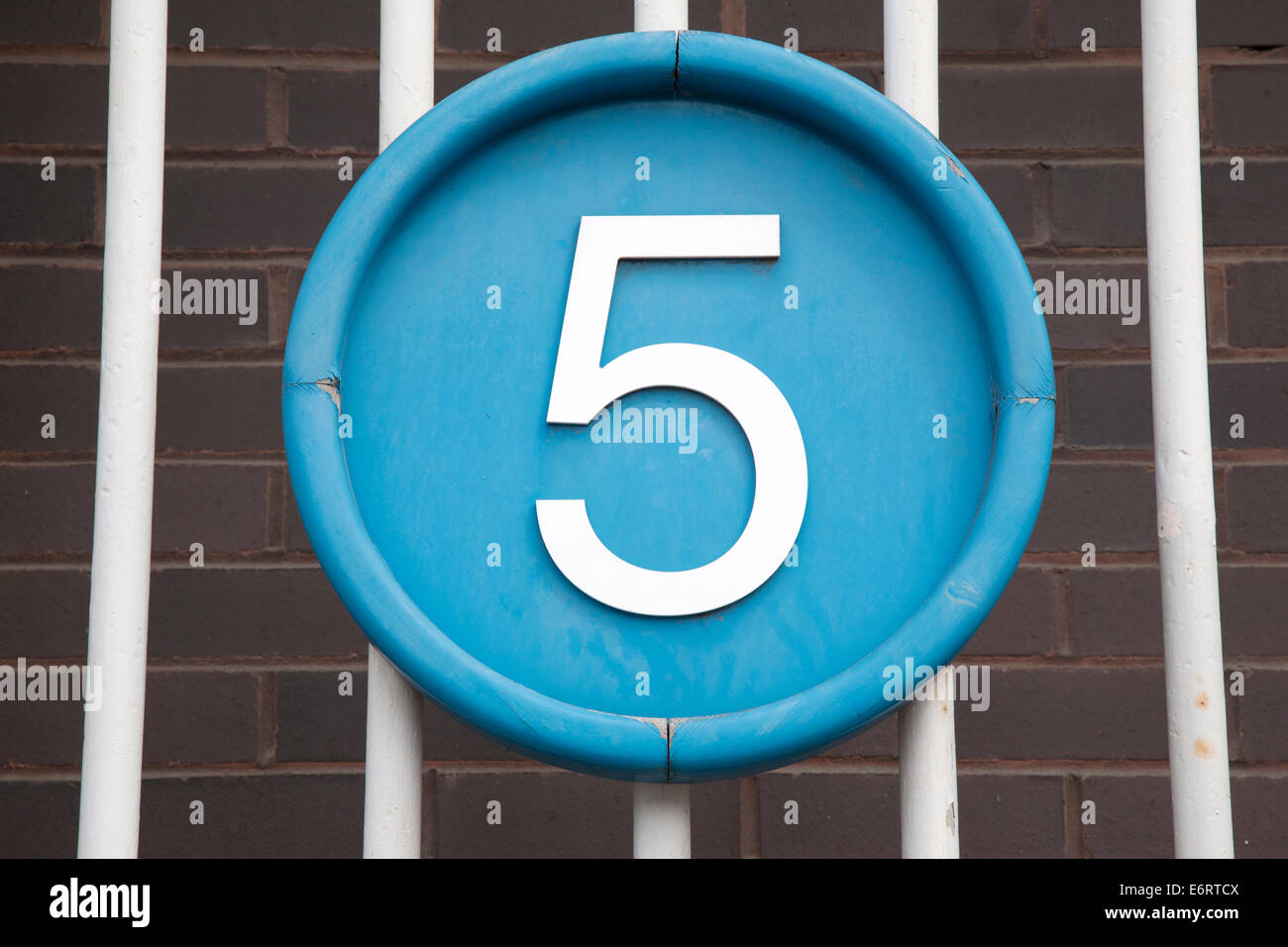 Number Five on Blue Circle against Brick Wall and Railings Background ...