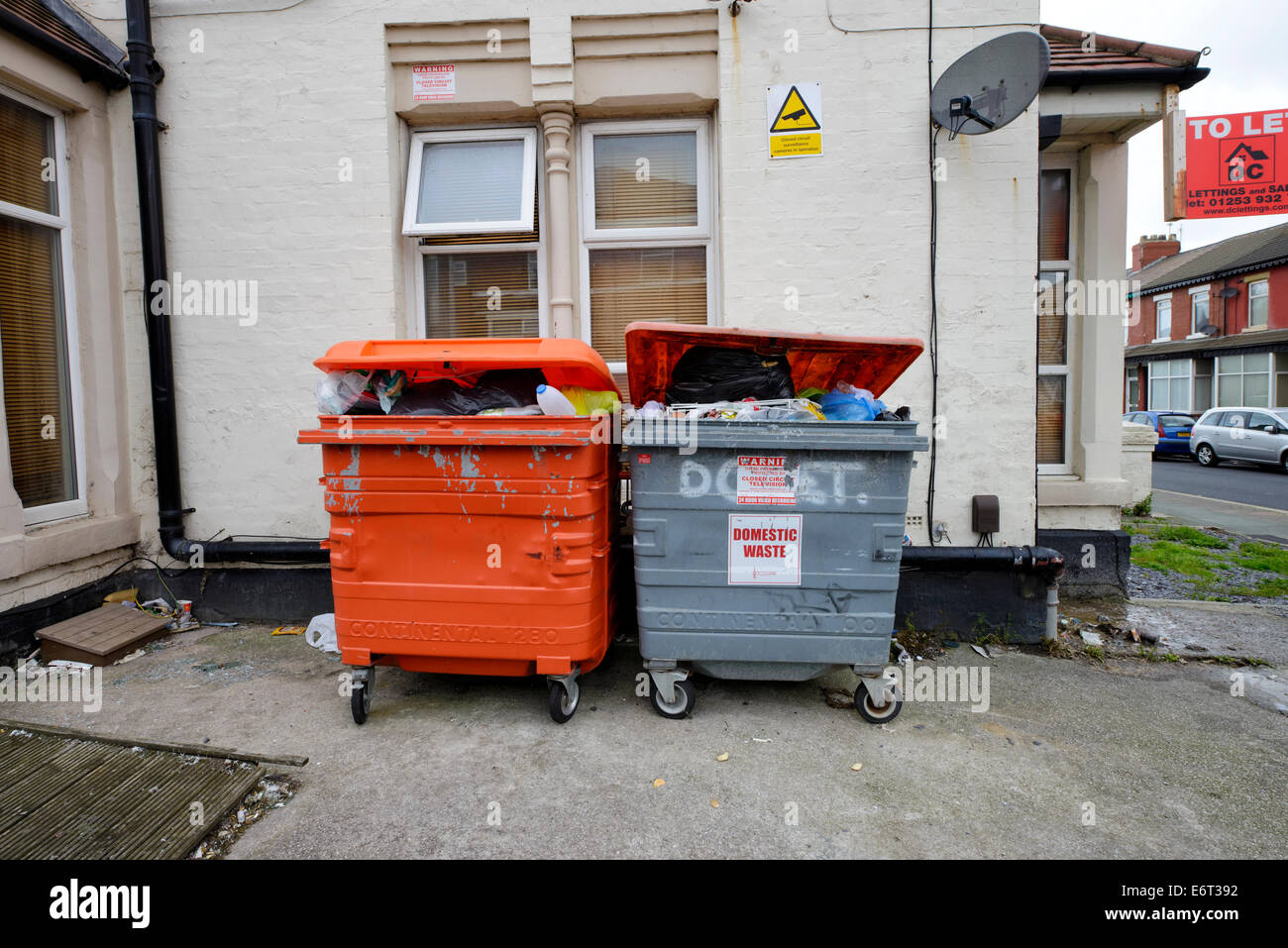 Overflowing domestic waste skips outside a house of multiple occupancy Stock Photo