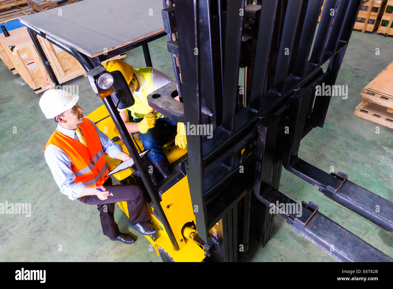 Asian Fork Lift Truck Driver Discussing Checklist With Foreman In